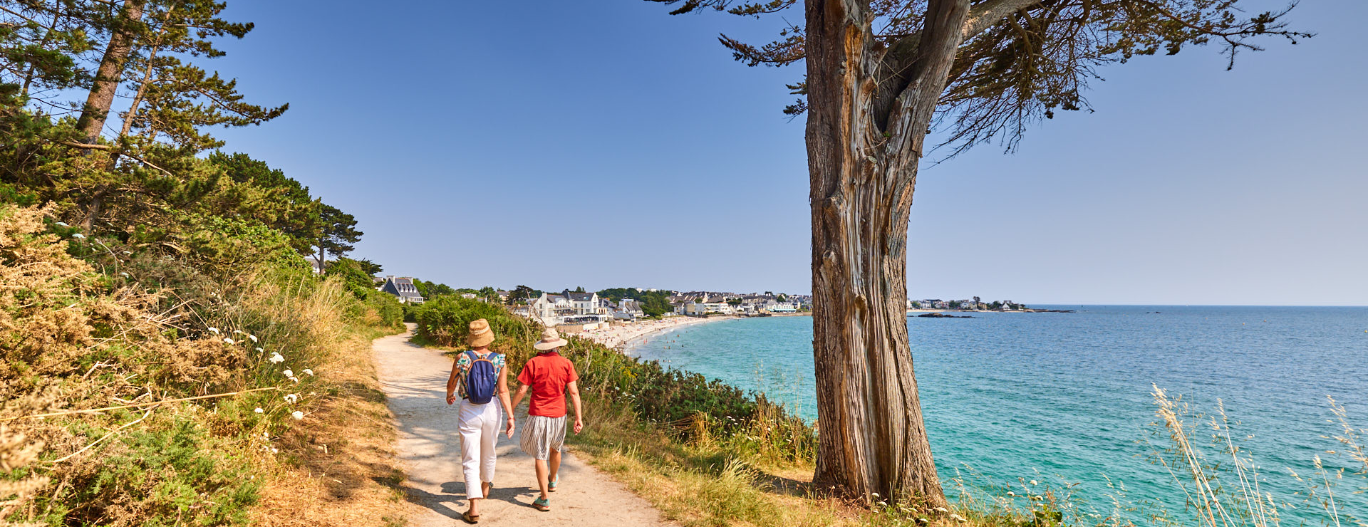 Deux randonneurs sur le GR34 à Concarneau. Vue sur la plage des Sables Blancs au loin.